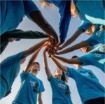 A group of RAs wearing matching blue shirts put their hands together in a circle formation.